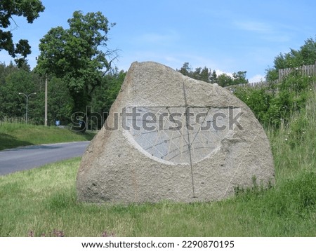Sundial made from a large piece of stone. A device for telling time by the apparent motion of the sun. We see them on a rock standing by the road at the edge of the village.