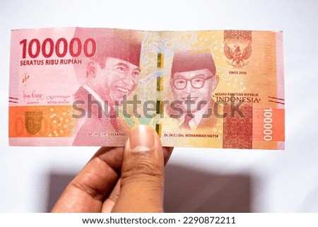 a man's hand is making a payment. Male hand showing Indonesian rupiah note. Indonesian Rupiah the official currency of Indonesia. Uang 100000 Rupiah Bank Indonesia. isolated on white background. Royalty-Free Stock Photo #2290872211