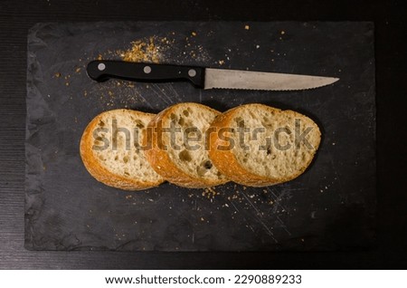 Slices of bread with crumbs and a knife on a black board background. View from above. World homemade food.