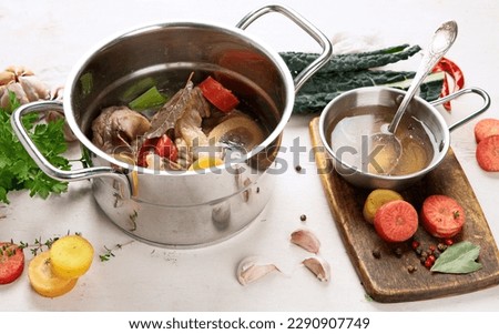 Beef broth of beef meat on bones slow cooked with vegetables: carrot, onion, garlic, and spices served in a pot on a white background with ingredients, top view.