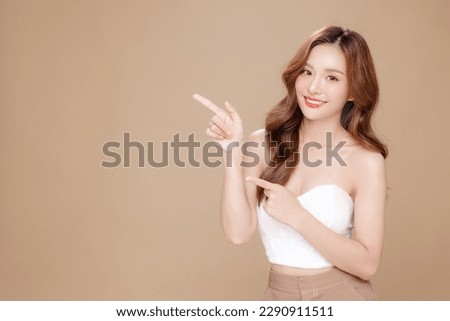 Young Asian beauty woman curly long hair with korean makeup style on face and perfect skin pointing to copy space on isolated beige background. Facial treatment, Cosmetology, plastic surgery.