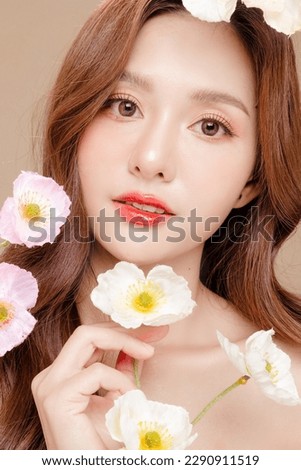 Young Asian beauty woman curly long hair with korean makeup style on face and perfect skin holding flower on isolated beige background. Facial treatment, Cosmetology, plastic surgery.
