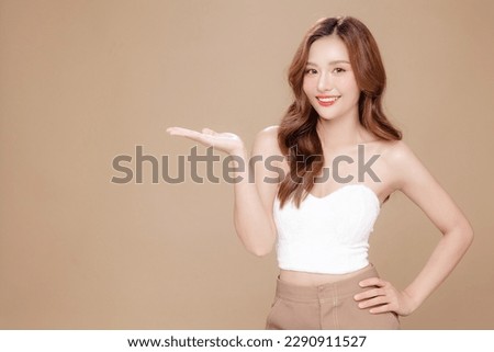 Young Asian beauty woman curly long hair with korean makeup style on face and perfect skin show copy space on her hand on isolated beige background. Facial treatment, Cosmetology, plastic surgery. Royalty-Free Stock Photo #2290911527