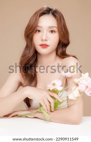 Young Asian beauty woman curly long hair with korean makeup style on face and perfect skin holding flower on isolated beige background. Facial treatment, Cosmetology, plastic surgery.