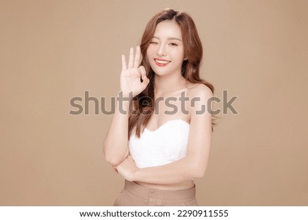 Young Asian beauty woman curly long hair with korean makeup style on face and perfect skin showing OK sign on isolated beige background. Facial treatment, Cosmetology, plastic surgery. Royalty-Free Stock Photo #2290911555