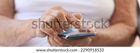 Close-up of old woman holding modern smartphone in hands. Grandma using cellphone. Communication with relatives, old age and senility concept Royalty-Free Stock Photo #2290918533
