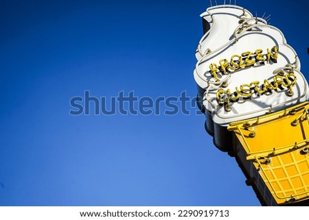 signboard of a ice cream shop says "frozen custard" on the edge, blue sky as background, santa monica pier, los angeles, california