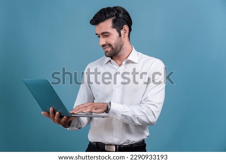 Successful businessman in black suit with innovative tech concept, standing pose and holding laptop and smiling with excitement on copyspace background for promotion or advertisement. Fervent