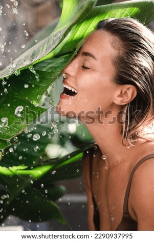 Young cheerful woman with tropical banana leaves and water splashes