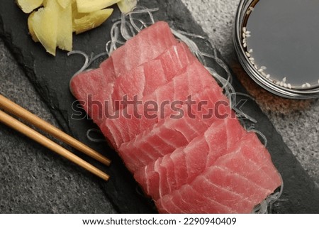 Tasty sashimi (pieces of fresh raw tuna), glass noodles, soy sauce and chopsticks on gray table, flat lay