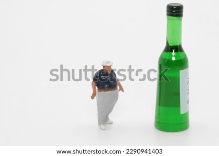 miniature figurine of an obese man with a giant beer bottle on a white background 