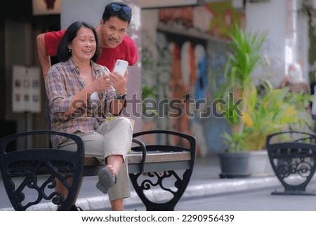 A seated woman is showing something on the phone to a man behind her