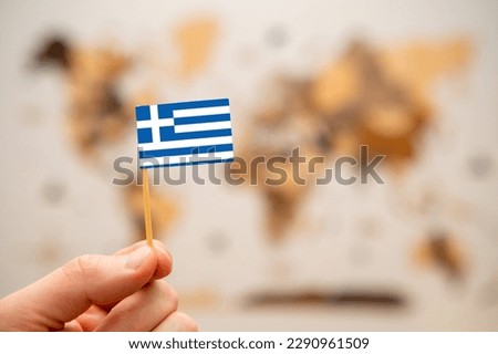 Greece flag in mans hand on the wooden world map background. Global economy and geopolitics concept. 
