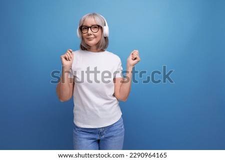 mature lady with gray hair listens to music in wireless headphones on studio background with copy space