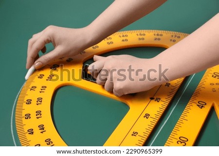 Woman drawing with chalk, triangle ruler and protractor on green board, closeup