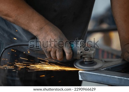 Profesional fabric worker cutting metal profile on the work table with an electric grinder in the industrial workshop.