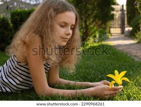 portrait of beautiful teenage girl 12 years old, lying on grass on sunny day, daydreaming, looking at a flower in her hands. enjoyment of rest, holidays. Joyful summer, happy childhood, good mood Royalty-Free Stock Photo #2290968261