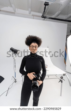 joyful african american content manager with digital camera near spotlight and shooting table in modern photo studio