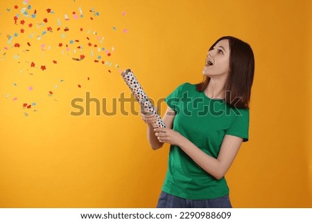 Happy teenage girl blowing up party popper on orange background Royalty-Free Stock Photo #2290988609