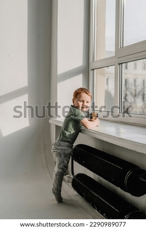 Adorable toddler boy playing with toy car at home, having fun isolated on white background studio, copy space. Child play with colorful toy. Little kid standing on floor near windows in sunny room.