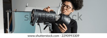 stylish african american content maker in eyeglasses working with professional lighting equipment in photo studio, banner