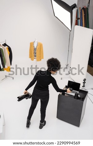 high angle view of african american photographer with digital camera holding photo lens near laptop in modern photo studio