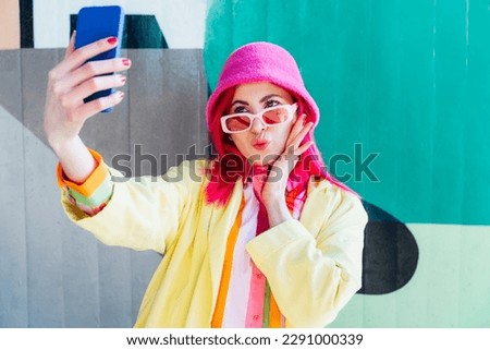 Excited pink hair woman taking a selfie photo outdoors. Emotional hipster fashion woman in bright clothes, pearl pink sunglasses, bucket hat taking selfie photo on the phone camera