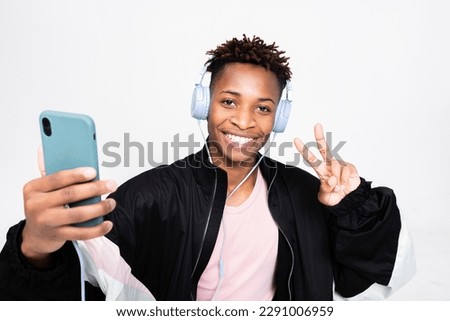 Cheerful attractive dark skinned guy hipster student man standing over white background in studio isolated smiling holding smartphone cell phone in hands taking picture while having shooting process.