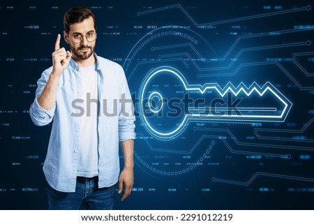 Attractive young european businessman pointing up at glowing key hologram on blurry background. Virtual house and future concept