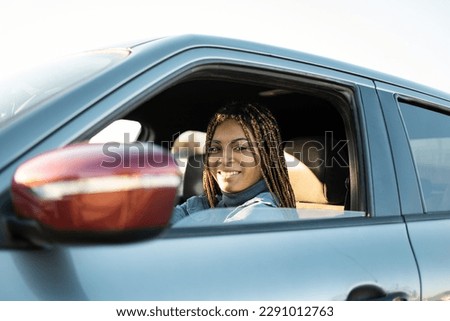 Dark-skinned young woman with braids sitting in a car looking at the camera smiling. Testing a new car, novice drivers, buying cars. Travel concept of young African women.