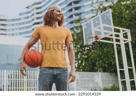 Young minded man 20s wearing yellow t-shirt bandana hold ball look aside playing basketball on playground in free time walking rest relax in city outdoors on open air. Urban lifestyle leisure concept