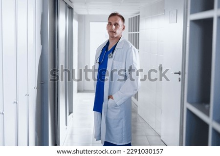 Portrait of a man in a blue surgical suit and a white coat in a hospital locker room.