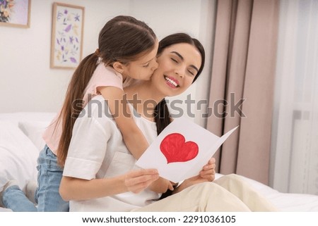 Happy woman with her daughter and handmade greeting card on bed at home. Mother's day celebration