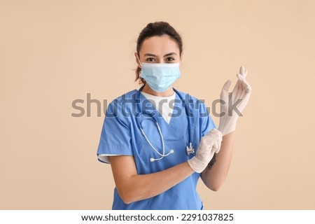 Female medical assistant putting on rubber gloves against beige background