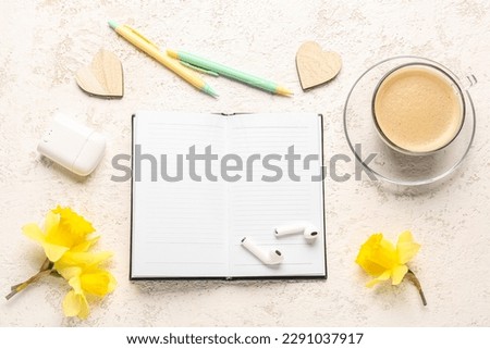 Composition with notebook, cup of coffee, earphones and narcissus flowers on white table