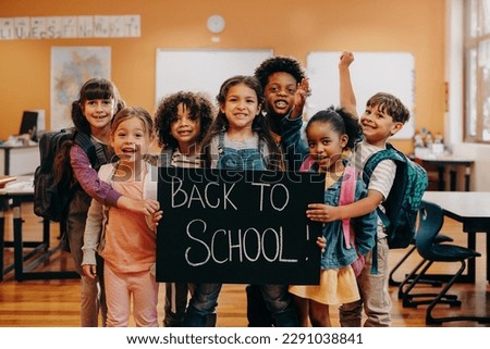 Back to school celebration. Excited elementary school class ready to learn on first day of class. Group of children smiling at the camera while holding a back to school sign in a classroom.