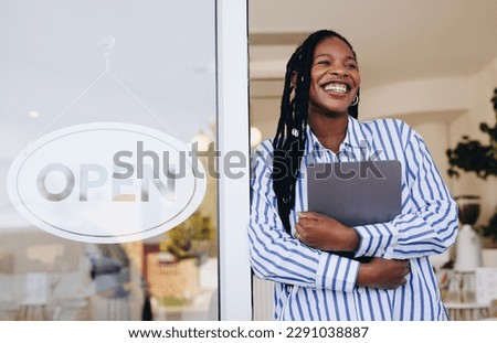 Successful young cafe owner standing next to an open sign at the entrance of her new restaurant. Female small business owner smiling happily while holding a digital tablet in her coffee shop.