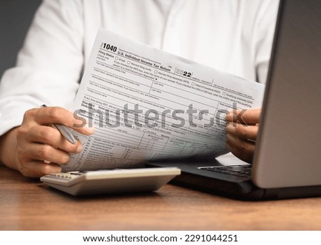 Tax day concept. Hand holding of form 1040. U.S. individual income tax return while sitting at the table in the office. Close-up photo Royalty-Free Stock Photo #2291044251