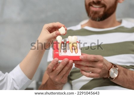 Doctor showing patient educational model of dental implant in clinic, closeup Royalty-Free Stock Photo #2291045643