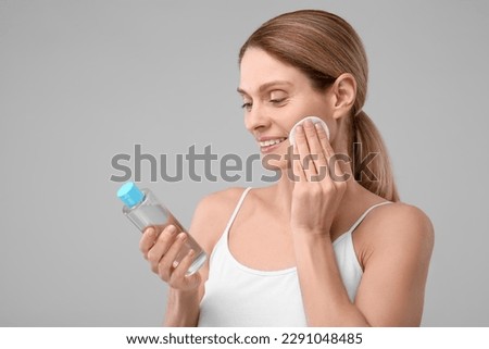 Beautiful woman removing makeup with cotton pad on gray background, space for text