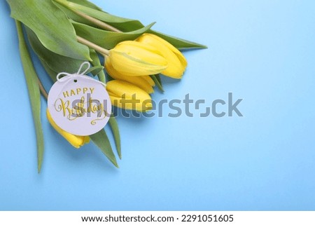 Beautiful tulip flowers with Happy Birthday card on light blue background, space for text
