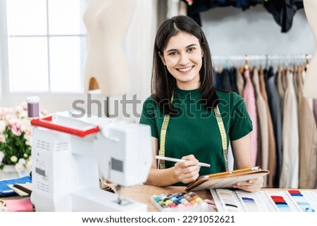 Smiling caucasian female fashion designer works in studio by idea drawing sketches with digital tablet and colorful fabric for a dress design collection, choose clothing colors for tailoring