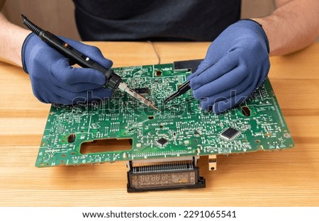 A man holds a soldering iron in his hand and solders a microcircuit Royalty-Free Stock Photo #2291065541