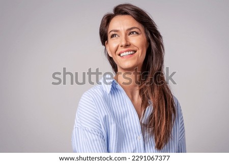 Smiling brunette businesswoman sitting against gray background. Confident female professional is wearing blue shirt. She is having brown hair. Copy space. Royalty-Free Stock Photo #2291067377