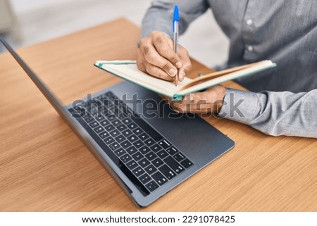 Young hispanic man writing on notebook at office