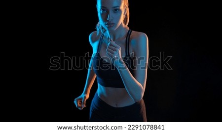 Sprinter run. Strong athletic woman running on black background with neon lights wearing in the sportswear. Fitness and sport motivation. Runner concept.