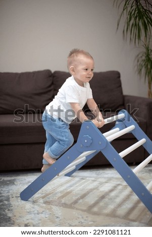 The boy climbs the wooden stairs - at home. A cute kid performs gymnastic exercises on the stairs. Children's sports wooden ladder. Physical education of children at home.