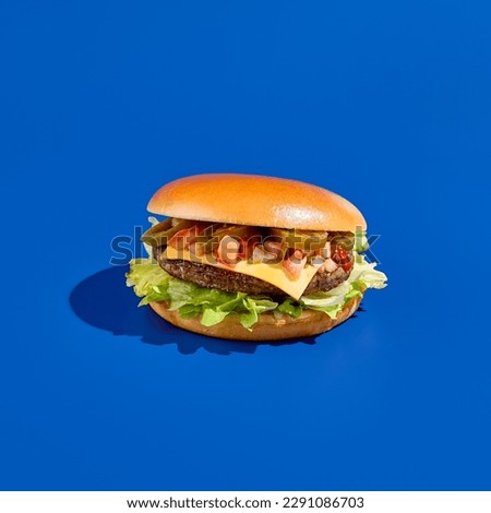 Juicy beef burger with jalapeno and fresh greens on a blue background. Modern, minimalist food photography in a square composition. Perfect takeout meal.