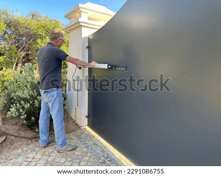 Man examining the hydraulic ram on an electric gate to a driveway Royalty-Free Stock Photo #2291086755