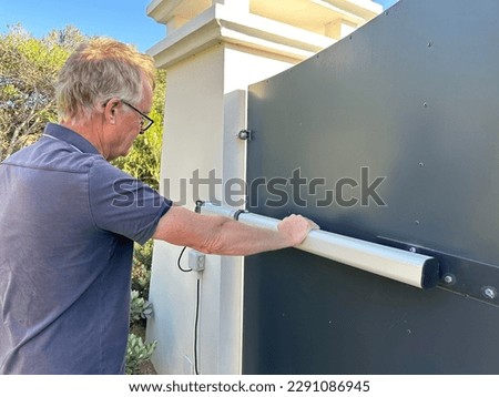Man examining the hydraulic ram on an electric gate to a driveway Royalty-Free Stock Photo #2291086945